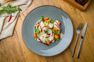 salad with pumpkin, cheese and herbs on grey plate on wooden table