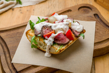 Bruschetta with roast beef, tomatoes, aragula and sause on woode board