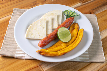 Arepa with chorizo, fried banana, lemon, traditional Colombian food, on wooden background