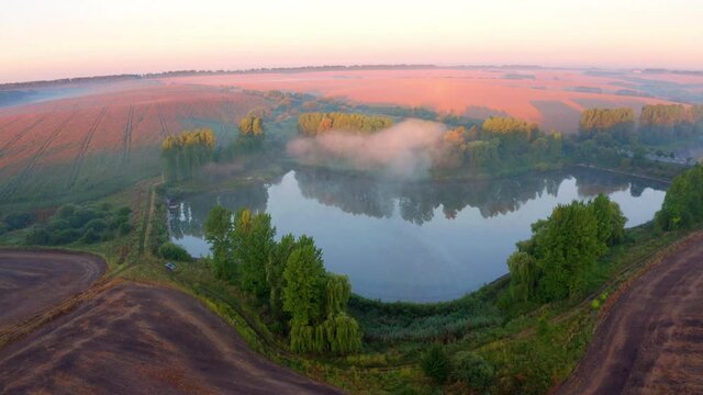 4K aerial - a bird's eye view&nbsp;video (Ultra High Definition). Summer sunrise on Ternopil outskirts with lake and asphalt road. Foggy morning view of hte Ukrainian countryside with field of wheat..