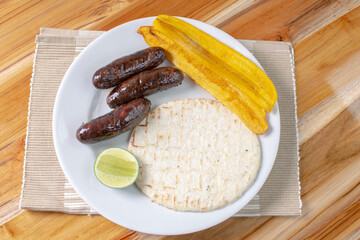 Arepa with blood sausage, fried banana, lemon, traditional Colombian food, on wooden background
