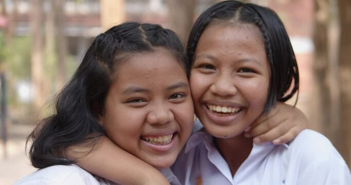 Slow motion scene of two young native Asian female student girls in white uniform who had pimple on their foreheads are laughing happily and joyful together on the natural bokeh background.