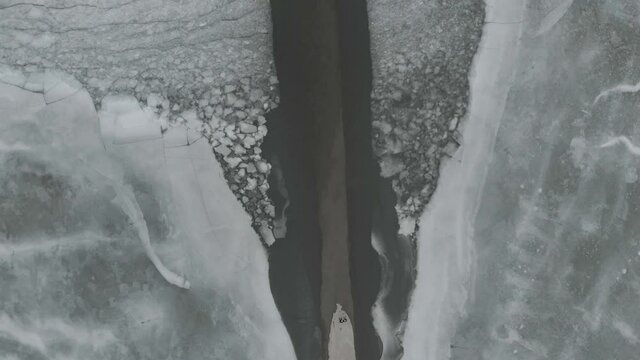 Top Down Drone Shot Over Melting Lake Ice With Underwater Road With Two People On The End Of The Road