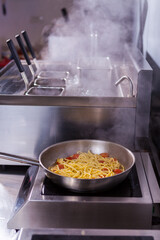 Cooking spaghetti concept. Pasta in the pan. Cooking Fresco Pasta.  Italian cuisine, tomato sauce for pasta, healthy food making, detailed view steam in the kitchen. Flipping pasta in the air