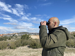 Man looking through binoculars in the field. Man watching. Man spying. Man watching birds in the field