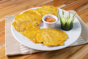 Patacon with stew, fried banana, decorated in white plate on wooden background
