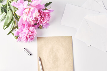a bouquet of pink peonies on office desk. notebook, envelope, pen and a coffee mug. feminine workplace, top view, copy space