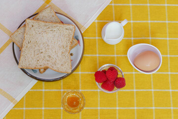 Ingredients for baking, egg milk bread honey and raspberries fruit. Cooking flat lay with copy space yellow blackground.