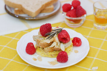 Homemade sweet bread pudding dessert with honey and raspberries in white dish on yellow table blackground.