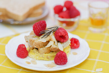 Homemade sweet bread pudding dessert with honey and raspberries in white dish on yellow table blackground.