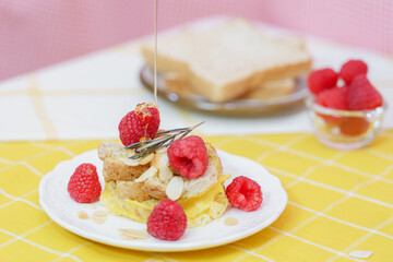 Homemade sweet bread pudding dessert with honey and raspberries in white dish on yellow table blackground.