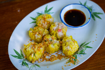 Chinese steamed dumpling with sauce in white dish on wooden table blackground.