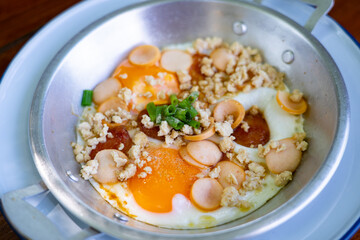 Thai food Pan Fried Egg with toppings   , sausage, minced pork in pan on wooden table blackground.