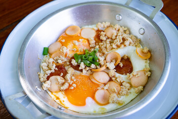 Thai food Pan Fried Egg with toppings   , sausage, minced pork in pan on wooden table blackground.