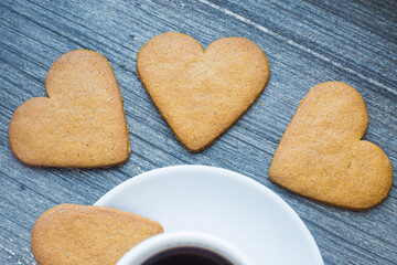 three gingerbread heart shaped biscuits near border of white porcelain coffee cup. Coffee break with love. Homemade sweets. Moments of tenderness. Postcard and wallpaper picture. 