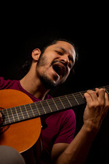 Obraz premium Man playing guitar and singing with black background
