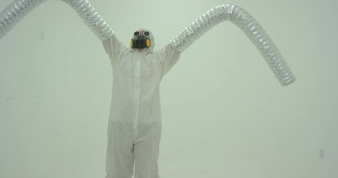 Strange silhouette of man in chemical protection suite with very long sleeves looking like monster hands dancing in front of white wall. Slow motion