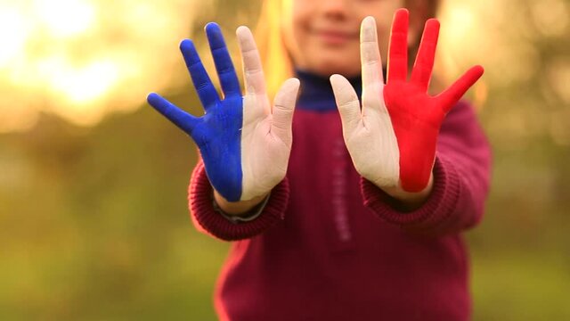 Joyful girl waving hands painted in France flag colors and say hello outdoor at sunset background
