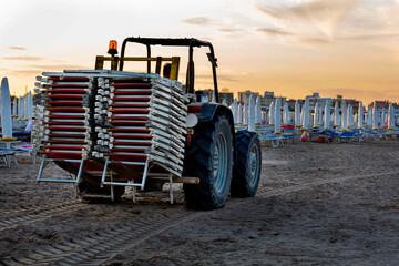 Obraz premium The tractor carries the sun loungers removed from the beach in the evening