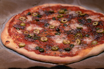 Freshky baked, homemade pizza Napoli laid on baking paper right after coming out of oven. Olives, anchovies, tomatoes. mozzarela.