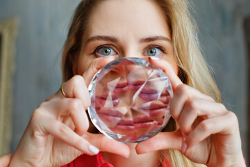A girl holds a crystal crystal with many reflections in front of her face