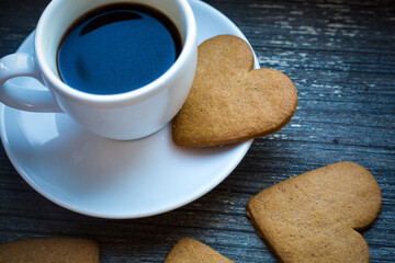 White coffeecup with hot fresh beverage and heart-shaped gingerbread biscuits. Coffee break with love. Side of coffee cup with hot beverage. Homemade sweets. Postcard and wallpaper picture. tradition