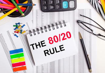 On the table there are reports, a calculator, colored pencils and stickers, a pen and a notebook with the text THE 80 20 RULE
