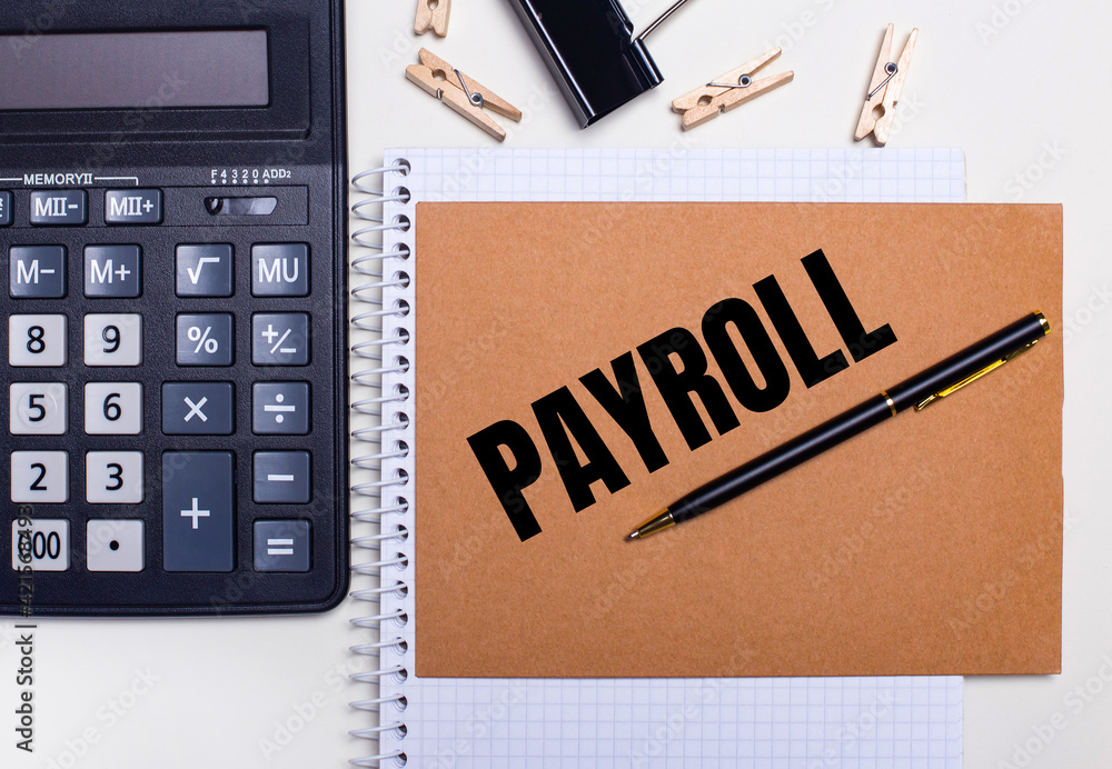 Poster on the desktop is a calculator, a pen and clothespins near a notebook with the text payroll. busines