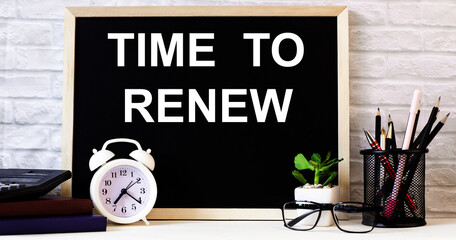 The words TIME TO RENEW is written on the chalkboard next to the white alarm clock, glasses, potted plant, and pencils in a stand.