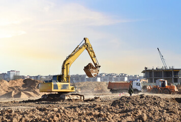 Excavator digging sand and loading into dump truck on construction site. Backhoe digs the ground,...