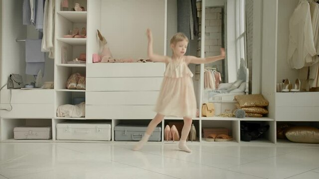 Dancing little girl enjoy new dress in clothing room on backdrop of wardrobe with clothes. Childhood, fashion and style
