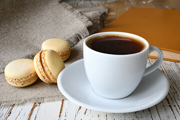 Сup of coffee, makroons and a book on the table.