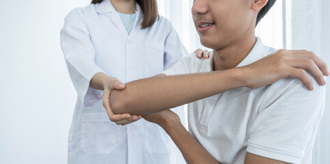 Female doctor doing physical therapy By extending the shoulder of a male patient