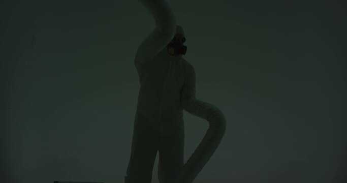 Strange silhouette of man in chemical protection suite with very long sleeves looking like monster hands dancing in front of white wall. Slow motion