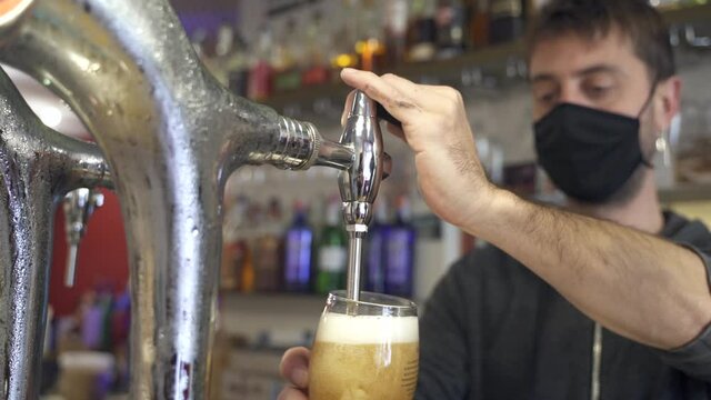 Bartender wearing face mask pouring and serving draft beer drink in a bar during the Coronavirus Pandemic