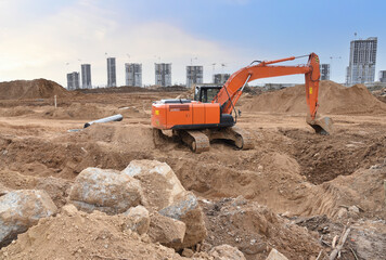 Obraz premium Excavator on earthworks at construction site. Backhoe on earthmoving and foundation work. Heavy machinery and equipment.
