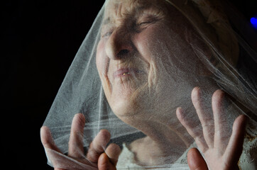The face of an old woman in a veil. The grandmother is trying to get out from under the shroud. The...