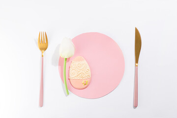 Easter eggs cookies with tulip and cutlery on pink paper circle as plate, holiday concept