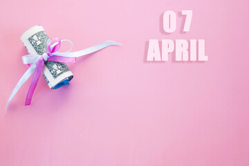 calendar date on pink background with rolled up dollar bills pinned by pink and blue ribbon with copy space.  April 7 is the seventh day of the month