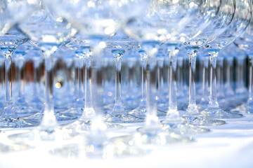 A lot of clean crystal glasses on white tablecloth prepared for big party. Blurred. Catering and restaurant utensils. wedding organisation. Wine tasting. Background picture. Group of objects 