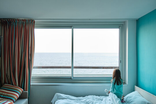 Une petite fille regarde la mer à travers la fenêtre d'une chambre d'hôtel