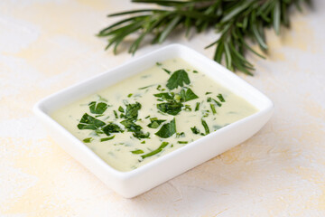 Bowl of Mayonnaise sauce and rosemary on yellow cement background.Side view
