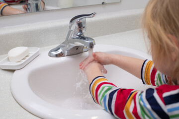 Child washing hands with soap in the bashroom