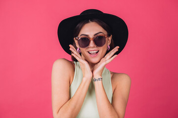 Beautiful stylish woman in hat and sunglasses posing over pink red background happy amazed excited  emotions, isolated copy space