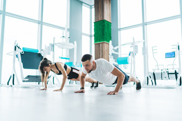 Fototapeta na wymiar Young active couple doing push ups in gym