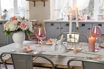 Closeup view of a dreamy table decor with glasses flowers and lit candles. Wedding easter birthday holiday table setup in a kitchen