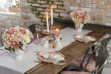 Side view of romantic cute table decor with glasses flowers and lit candles. Wedding easter birthday holiday setup on a wooden table