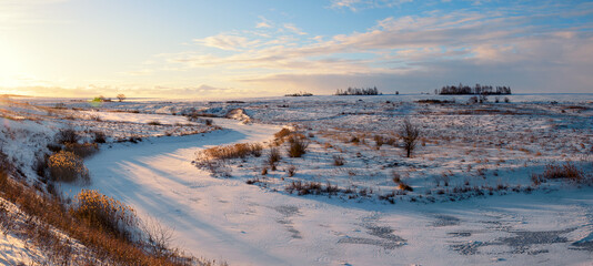 Sunny panoramic early springtime landscape.Beautiful view of frozen river and snow covered fields during sunny march morning.