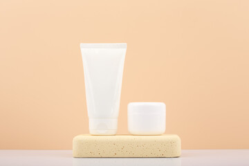 White cream tubes with cosmetic products on beige stone podium against beige background with copy...