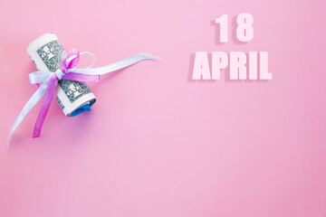 calendar date on pink background with rolled up dollar bills pinned by pink and blue ribbon with copy space. April 18 is the eighteenth day of the month